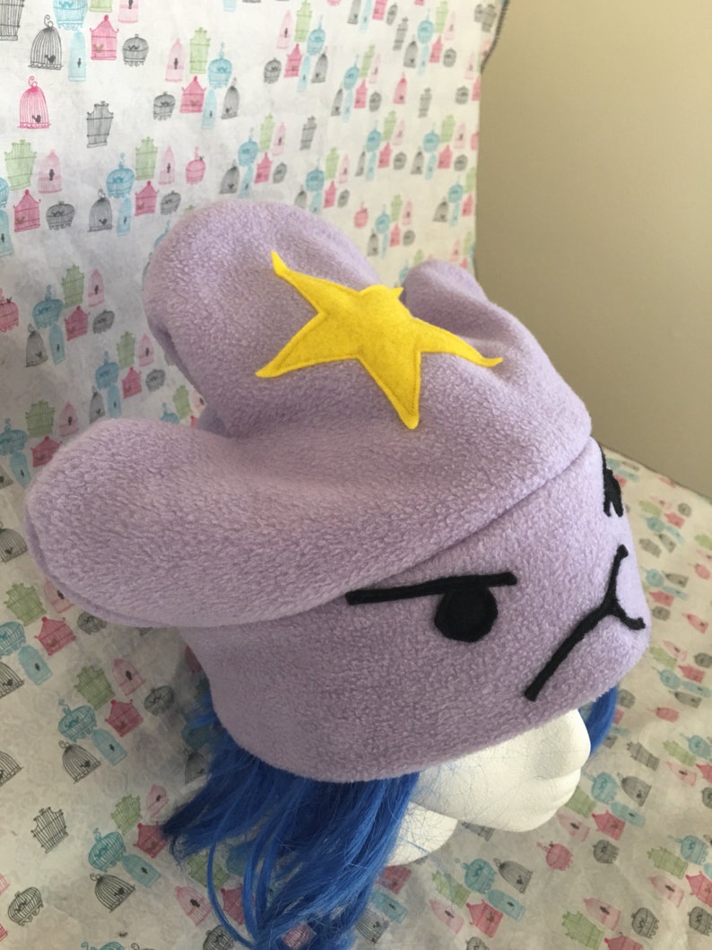 May include: Purple fleece Lumpy Space Princess hat with a yellow felt star and embroidered black facial features. The hat is shown on a mannequin head with blue wig.  The hat is a handmade, wearable costume accessory, perfect for fans of Adventure Time.