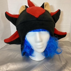May include: Black fleece hat with red and tan accents, shaped like a hedgehog with spikes. The hat is worn on a mannequin with blue hair.