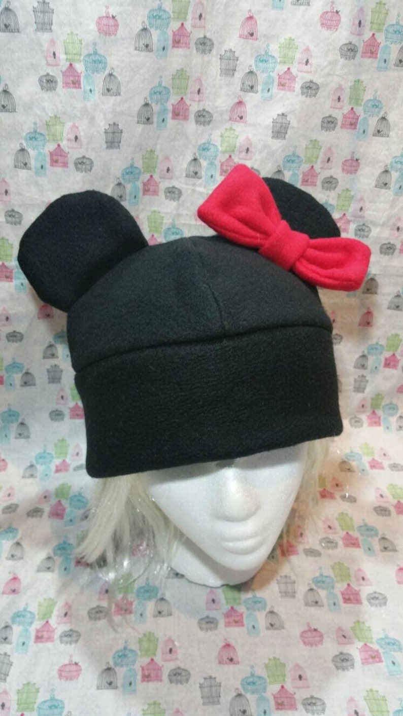 May include: Black fleece hat with large, rounded ears and a red bow on top. The hat is on a mannequin head.