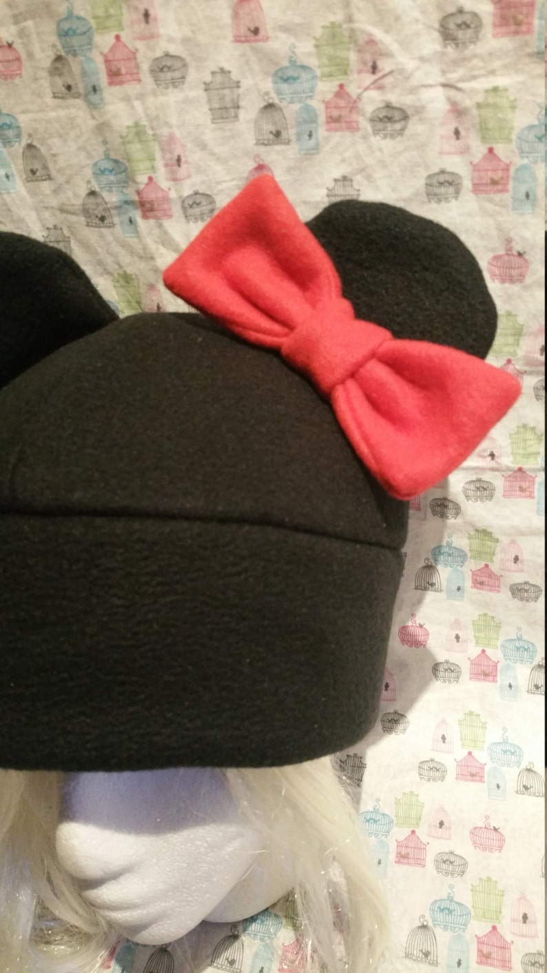 May include: Black fleece hat with large, floppy red bow and mouse ears.