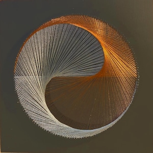 Op de afbeelding: Een cirkelvormig draadkunstwerk met een yin-yang ontwerp. Het kunstwerk is verdeeld in twee helften: de ene kant heeft witte draad en de andere kant oranje draad. De achtergrond is donkergrijs.