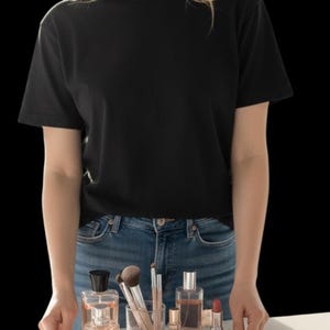 Puede incluir: Una camiseta negra de cuello redondo y vaqueros azules. Una bandeja redonda transparente con ribete dorado contiene frascos de perfume, brochas de maquillaje, l&aacute;piz labial y polveras. La bandeja est&aacute; decorada con flores.
