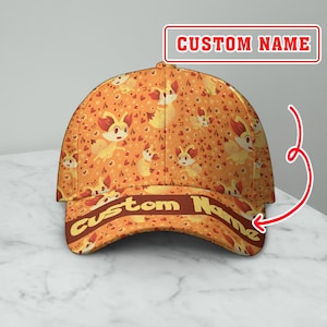 May include: Orange baseball cap with a repeating pattern of cartoon characters, hearts, and stars. The brim features the text "Custom Name" in a brown font. The text "Custom Name" is also displayed in a red box.