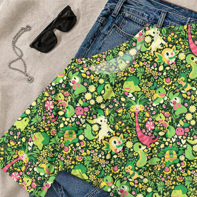 May include: A short-sleeve t-shirt featuring an all-over print of various green and yellow cartoon creatures interspersed with small flowers, leaves, and hearts on a dark green background, paired with blue denim jeans, black sunglasses, and a silver chain.