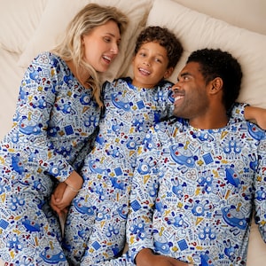 May include: Matching long-sleeve pajama sets featuring a white background with a repeating blue and multicolored pattern of cartoon robots, calculators, geometric shapes, and the word MATH printed in bold capital letters across the fabric.