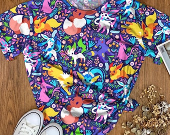 May include: A short-sleeve t-shirt featuring an all-over print of various colorful cartoon creatures, including fox-like and rabbit-like characters, interspersed with vibrant floral and leafy patterns against a dark purple background.