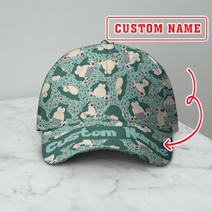 Puede incluir: Gorra de béisbol turquesa con un patrón repetido de personajes de dibujos animados. La gorra tiene una visera curva y el texto "Custom Name" es visible. El fondo es gris claro.