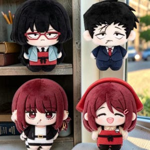 Op de afbeelding: Vier pluche poppen met gestileerde, op anime geïnspireerde personages. De pop linksboven heeft zwart haar en een rode bril. De pop rechtsboven draagt een pak. De twee onderste poppen hebben kastanjebruin haar en dragen verschillende kledingstukken.