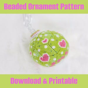 May include: A green beaded Christmas ornament with pink hearts and white dots. The ornament is hanging from a clear string. The text "Beaded Ornament Pattern" is at the top of the image and "Download & Printable" is at the bottom.