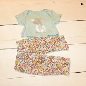 Puede incluir: Un conjunto de ropa para bebé con una camisa de manga corta azul claro con estampado de animales de dibujos animados y pantalones con estampado floral.