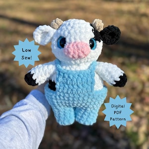 Puede incluir: Un peluche de vaca hecho a mano con ganchillo, de color blanco con manchas negras y ojos azules. Lleva un peto azul claro y tiene pequeños cuernos. El texto en la imagen dice "Low Sew!" y "Digital PDF Pattern".