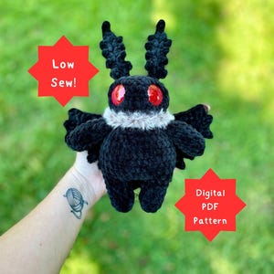 Puede incluir: Un peluche de polilla negra de ganchillo con ojos rojos y un cuello blanco esponjoso. El peluche tiene antenas y alas grandes y texturizadas. La imagen incluye el texto "Low Sew!" y "Digital PDF Pattern".