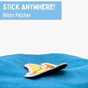 May include: A yellow and orange cartoon fish velcro patch on a blue fabric surface. The text "STICK ANYWHERE! Velcro Patches" is in the top left corner of the image.