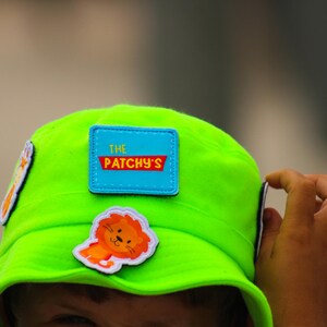 May include: A bright green bucket hat with a blue patch that says "The Patchy's" and a cartoon lion patch.