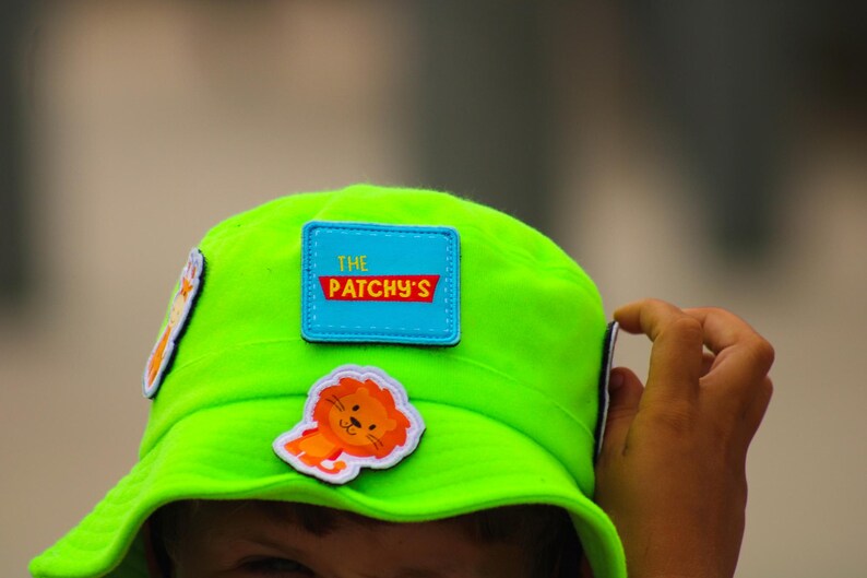 May include: A bright green bucket hat with a blue patch that says "The Patchy's" and a cartoon lion patch.