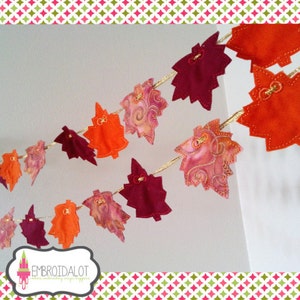 May include: A garland of felt leaves in shades of orange, red, and pink, with gold accents. The leaves are strung together with gold thread and are arranged in a cascading pattern.