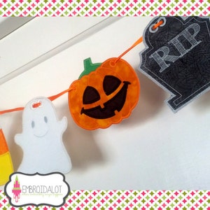 May include: A Halloween banner with a candy corn, a ghost, a jack-o'-lantern, and a tombstone with "RIP" stitched on it. The decorations are strung together with orange ribbon. The banner is set against a white background.