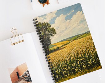 May include: A spiral-bound notebook featuring a landscape painting of a wheat field under a cloudy sky. The cover art depicts a tree, golden fields, and a blue sky. The notebook is open on a white surface.
