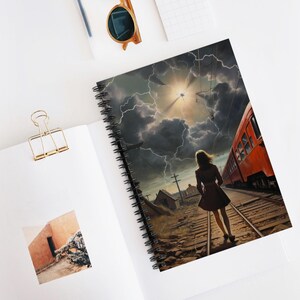 Può includere: Quaderno a spirale con una drammatica illustrazione di una donna che cammina sui binari del treno verso un treno rosso sotto un cielo tempestoso con fulmini. Il quaderno è aperto su una superficie bianca con una graffetta dorata e occhiali da sole.