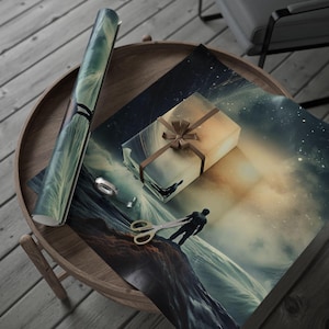 May include: A rolled-up gift wrap roll and a wrapped gift box with a brown ribbon sit on a wooden table. The gift wrap and box feature a surreal ocean and sky design. A pair of gold scissors and a silver ring are also on the table.