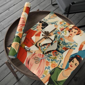Pode incluir: Um rolo de papel de embrulho em estilo vintage e uma caixa de presente embrulhada com uma fita castanha estão sobre uma mesa de madeira. O papel de embrulho apresenta ilustrações de mulheres em vestidos. Uma tesoura repousa sobre o papel.