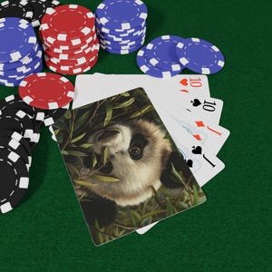 Op de afbeelding: Pokerset met speelkaarten en fiches. De speelkaarten hebben een panda-berendesign en het nummer 10. De fiches zijn rood, zwart en blauw. De achtergrond is een groene viltlaag.