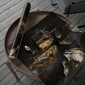 May include: A roll of black and gold wrapping paper, a wrapped gift with a bow, and sheets of paper with a medieval knight's helmet design. Gold scissors and tape dispenser are on a wooden table.