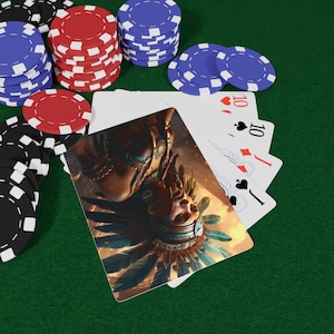 Puede incluir: Juego de póquer sobre una superficie de fieltro verde. El juego incluye montones de fichas de póquer rojas, azules y negras, cartas que muestran el número 10 y una carta con una ilustración de una persona con un tocado de plumas.