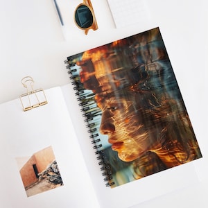 Könnte beinhalten: Spiralgebundenes Notizbuch mit einem künstlerischen Porträt eines Profils, verziert mit goldenen Lichteffekten. Das Notizbuch hat eine schwarze Spiralbindung und liegt offen auf einer weißen Oberfläche.