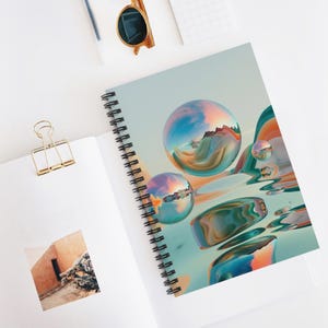 May include: Spiral-bound notebook with a colorful, abstract design featuring reflective orbs and flowing shapes in shades of blue, orange, and green. The notebook is open, revealing a blank page and a gold paper clip.