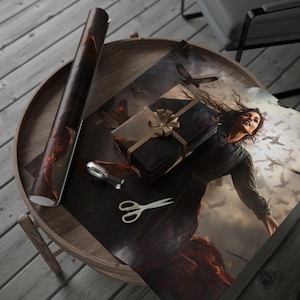 May include: A wooden table displays a roll of wrapping paper, a wrapped gift with a bow, and a sheet of paper with a fantasy art print. Gold scissors and a silver tape dispenser are also present. The art depicts a woman and flying birds.