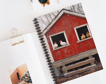 May include: Spiral-bound notebook featuring a vibrant image of a red barn with chickens in the windows. The notebook is open, revealing a blank page and a gold paper clip. A pair of sunglasses and a pen are also visible.