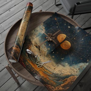 May include: A rolled-up vintage map and gift-wrapped box with a celestial map design sit on a wooden table. A pair of scissors and tape are also on the table. The gift box is tied with a brown ribbon.