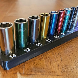 May include: A set of chrome sockets in various colors, ranging from gold to purple, arranged on a black holder. The sockets are labeled with numbers from 5 to 14, indicating their size. The tools are designed for mechanical work.