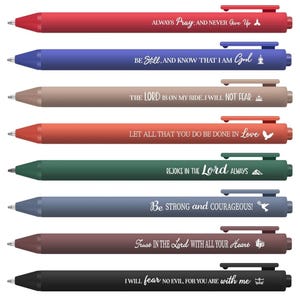 May include: A collection of eight ballpoint pens in various colors, including red, blue, brown, orange, green, and black. Each pen features a different inspirational quote in white lettering. The pens have a clip and a push-button mechanism.