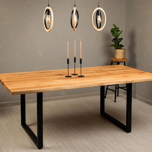 Puede incluir: Una mesa de comedor de madera con acabado natural y patas de metal negro. La mesa está puesta con cuatro candelabros negros y velas.