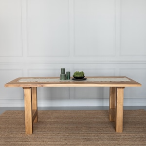 Könnte beinhalten: Rechteckiger Esstisch aus hellem Holz, ca. 180 cm lang. Auf dem Tisch befinden sich ein beiger Tischläufer, grüne Kerzen und eine schwarze Schale mit Grünzeug. Der Tisch steht auf einem braunen Teppich.