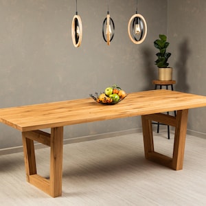 May include: A light wood dining table with a rectangular top and a unique, open, triangular base. The table is made of solid wood and has a natural finish. The table is set with a bowl of fruit and is surrounded by a light wood floor.