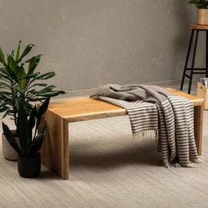 Puede incluir: Una mesa de centro de madera clara con un diseño de borde vivo. Una manta de rayas está colocada sobre la mesa.