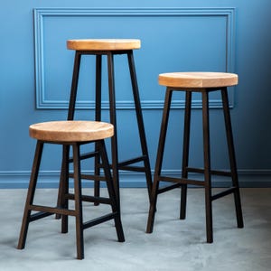 May include: Three wooden bar stools with black metal frames. The stools have a natural wood finish and are all different heights.
