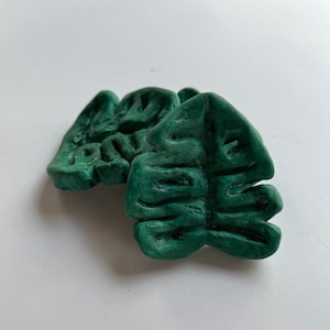 May include: Two green, sculpted, monstera leaf shapes made of clay.