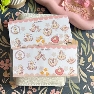 May include: Two rectangular sticker sheets labeled KIDS MONEY featuring various illustrations of cartoon ducks, including ducks in heart shapes, ducks with flowers, and yellow stars, with a scalloped pink border on a white background.