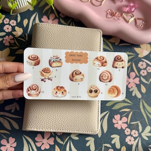 May include: A beige card with cinnamon roll illustrations and the text "SAVE THAT DOUGH". The card features various cartoon cinnamon rolls with different expressions and point values. The card is resting on a beige leather wallet.