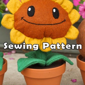 May include: A felt sunflower plush toy with a smiling face, green leaves, and a brown pot. The toy is sitting on a light grey surface. Sewing Pattern.