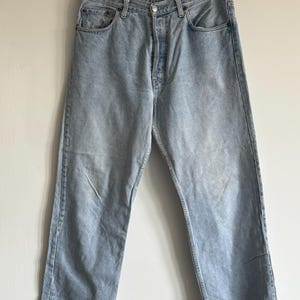 Pode incluir: Jeans de denim azul claro com fecho de botão e cinco bolsos.