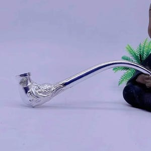 Puede incluir: Una pipa de fumar de plata con un diseño adornado en la cazoleta. La pipa tiene una boquilla larga y curva.