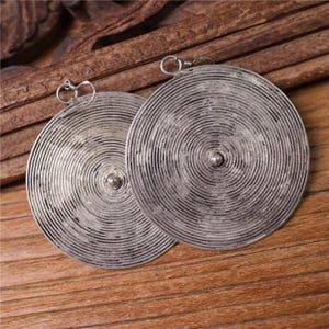 Pode incluir: Um par de brincos de prata com um design circular. Os brincos têm um padrão de círculos concêntricos texturizado.