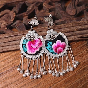 Puede incluir: Un par de pendientes de plata con diseños florales bordados en negro y rosa y cuentas de plata colgantes.