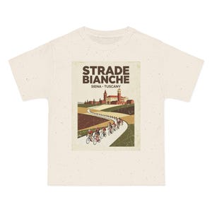 May include: Cream-colored t-shirt featuring a vintage-style graphic of the Strade Bianche cycling race in Siena, Tuscany. The design includes cyclists, a winding road, and Italian architecture. The text "STRADE BIANCHE" is prominently displayed.