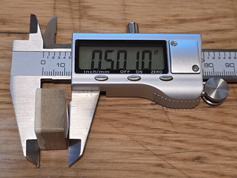 May include: A small, rectangular, light-colored block with a textured surface being measured by a silver digital caliper. The digital display on the caliper clearly shows a measurement of 0.50 inches, indicating the width of the object.